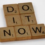 Wooden scrabble tiles forming 'DO IT NOW' on a minimal white backdrop. Inspiring concept.